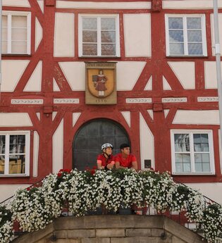 Zwei Personen stehen auf dem Treppenaufgang zum historischen Rathaus mit rotem Fachwerk