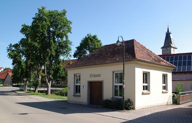Das Gebäude des historischen Eichamts Blaufelden mit Bäumen und dem Kirchturm im Hintergrund