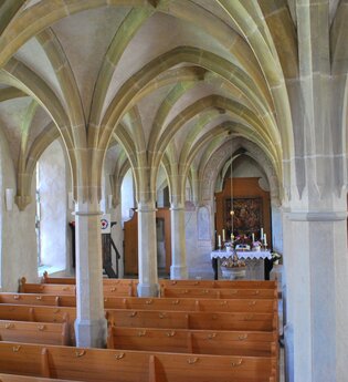 Blick in den Innenbereich der Klosterkirche Frauental. Es sind die Deckengewölbe und die Sitzreihen sowie der Altar zu sehen.
