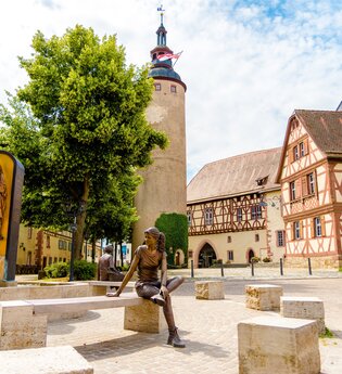 Blick auf den Schlossplatz in Tauberbischofsheim. Im Hintergrund ist der Türmersturm mit dem Kurmainzischen Schloss zu sehen. Im Vordergrund ein Brunnen mit Figuren aus Kupfer.