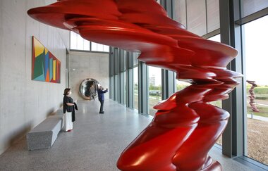 Zwei Besucher bewundern eine rote Skulptur und genießen den Ausblick ins Grüne