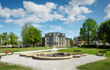 Neues Schloss in Gaildorf mit Brunnen im Vordergrund und blauem Himmel.