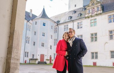 Ein Pärchen steht im Torbogen zum Schlossinnenhof. Im Hintergrund sieht man den Turm des Schlosses.