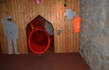 Blick auf einen Rutschenausgang in der Spielscheune in Röttingen. Der Ausgang ist mit einer Holzwand verkleidet. Ein gemalter Ritter hält daneben Wache.