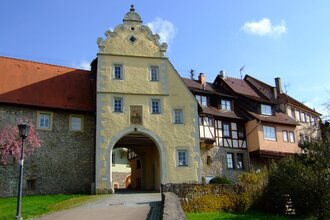 Das Tor ist gelb und hat einen Giebel. Daneben befinden sich Fachwerkhäuser auf der Stadtmauer