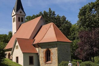 Zwei Radfahrer stehen vor einer Kapelle mit einem spitzen Turm