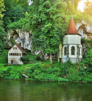 Die Wallfahrtskapelle steht am Fluss Jagst mit einer aufragenden Tuffsteinfelsenwand dahinter