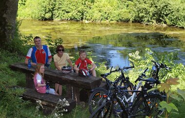 Eine Familie macht bei einer Radtour Rast auf einer Bank an der Jagst