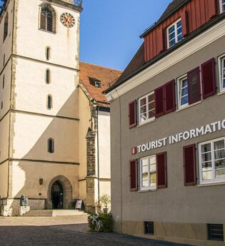 Tourist-Information neben einer Kirche mit Turm und roten Fensterläden.