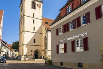 Tourist-Information neben einer Kirche mit Turm und roten Fensterläden.