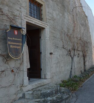Blick auf den äußeren Eingangsbereich des Weinmuseums in Röttingen. An der Wand hängt ein großes Ritter-Schutzschild mit der Aufschrift "Burg Brattenstein, Weinmuseum Röttingen" .