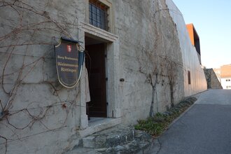 Blick auf den äußeren Eingangsbereich des Weinmuseums in Röttingen. An der Wand hängt ein großes Ritter-Schutzschild mit der Aufschrift "Burg Brattenstein, Weinmuseum Röttingen" .