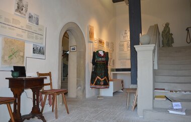 Blick in den Innenbereich des Weinmuseums in Röttingen. Hier ist eine Tracht sowie ein alter Sekretär mit Stühlen zu sehen. Eine Treppe führt in die zweite Etage.