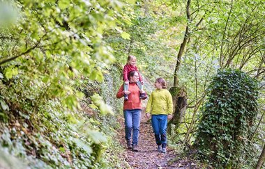Eine Mutter ist mit ihren beiden Kindern im Wald unterwegs.