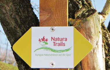 In der Wegmarkierung steht Natura Trails, Blumen und eine grüne Welle