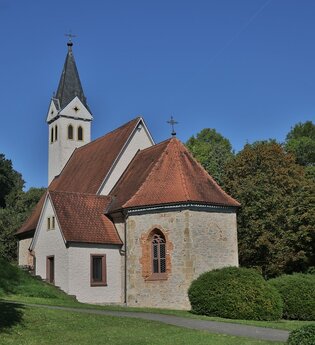 Die Kirche hat einen spitzen Turm und ist von grünen Bäumen umgeben