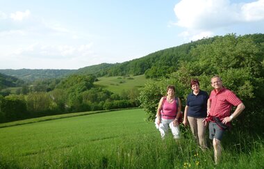 Zwei Frauen und ein Mann lstehen auf einer Wiese achen in die Kamera