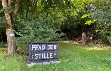 Ein Schild mit Schrift Pfad der Stille weist den Weg in den Steig