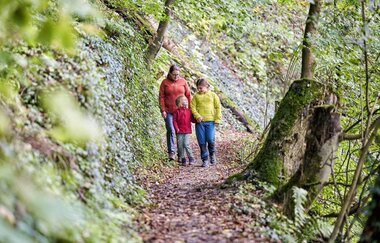 Eine Frau in roter Jacke  wandert mit ihren beiden Kindern im Wald