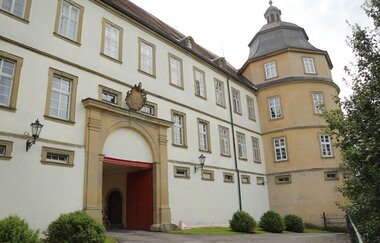 Das Schloss hat einen Turm und ein Wappen über dem weißen Eingang